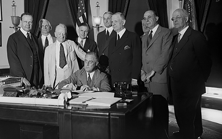 President Roosevelt signs the Glass-Steagall Act alongside the bill's co-sponsors, Senator Carter Glass and Representative Henry Steagall, and others.