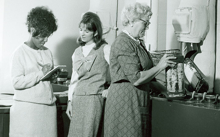 Black and white photo of Jacque Banks (left) and two other San Francisco employees along with one of the pneumatic tube cylinders used for inter-departmental messaging