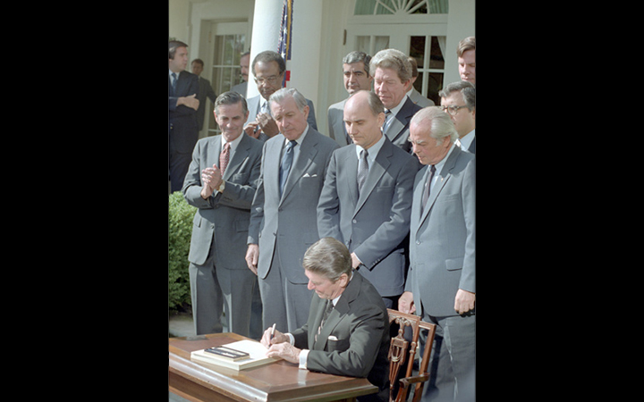 President Ronald Reagan signs the Garn-St. Germain Act in the White House Rose Garden surrounded by administration officials and members of Congress.
